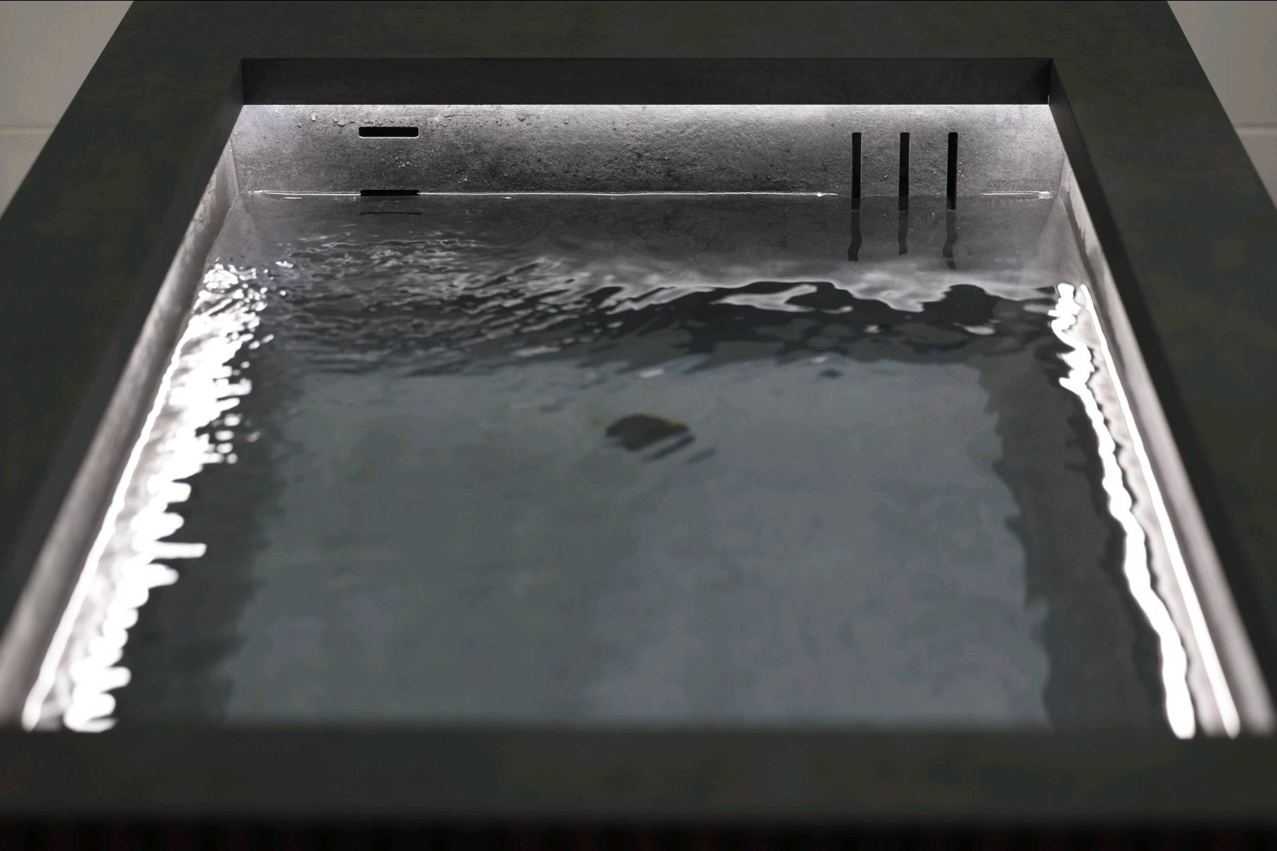 Close-up of the Ember and Ice Contrast Therapy Bath with water gently rippling in a dark stone basin and soft ambient lighting.