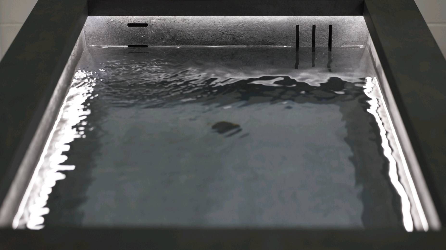 Close-up of the Ember and Ice Contrast Therapy Bath with water gently rippling in a dark stone basin and soft ambient lighting.