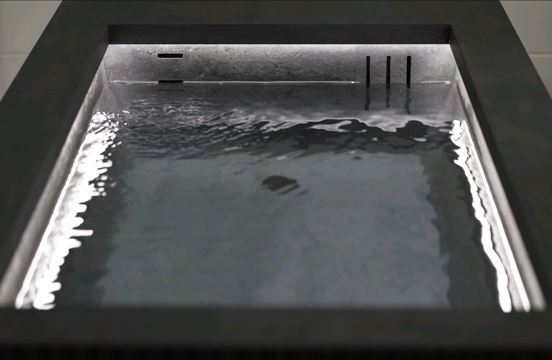 Close-up of the Ember and Ice Contrast Therapy Bath with water gently rippling in a dark stone basin and soft ambient lighting.