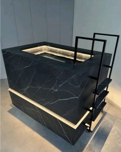 Thor Contrast Therapy Bath in black stone finish with white veining and integrated LED lighting, featuring a modern step ladder and clean architectural lines.