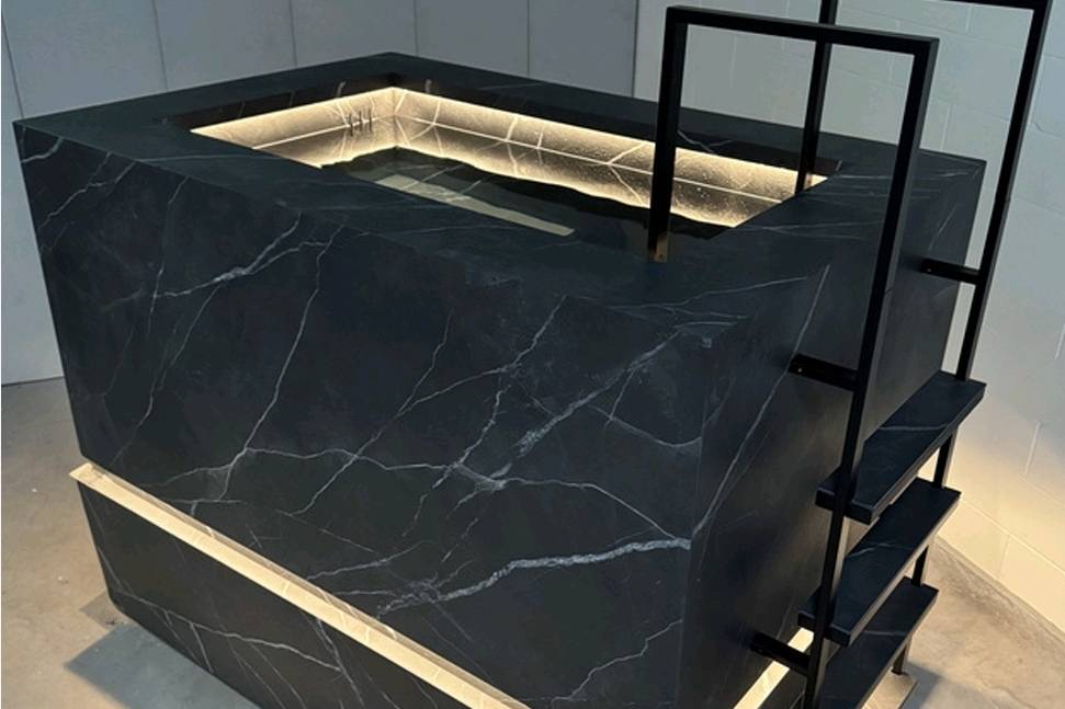 Thor Contrast Therapy Bath in black stone finish with white veining and integrated LED lighting, featuring a modern step ladder and clean architectural lines.