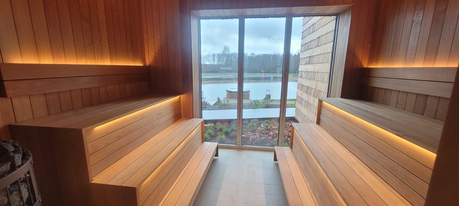 Indoor sauna featuring sleek wooden benches, soft LED lighting, and large windows overlooking a serene outdoor landscape, emphasizing modern design and wellness benefits.