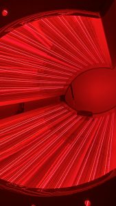 Ember and Ice full-body red light therapy bed glowing red inside a luxury wellness room with a lounge chair and ambient lighting.