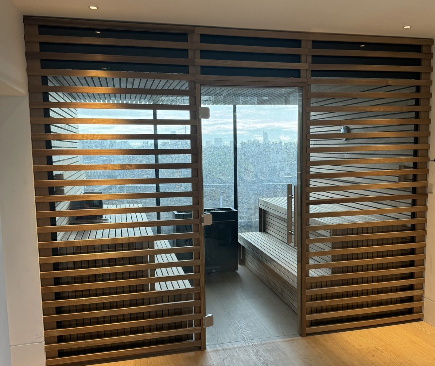 Luxury indoor sauna with modern wooden slat design, featuring a spacious interior and large windows for natural light, highlighting Ember and Ice's premium craftsmanship.