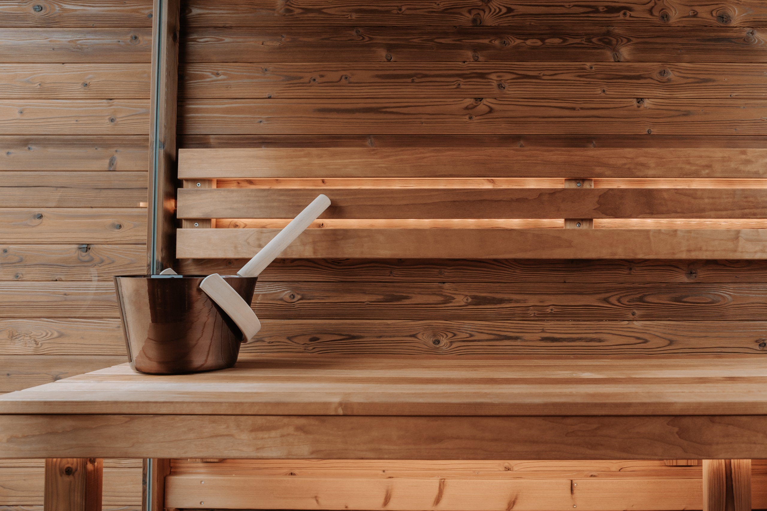 Wooden sauna interior featuring a metal bucket and ladle on a wooden bench, emphasizing wellness and relaxation themes.